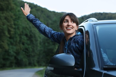 Smiling woman leaning out of car window in beautiful mountains