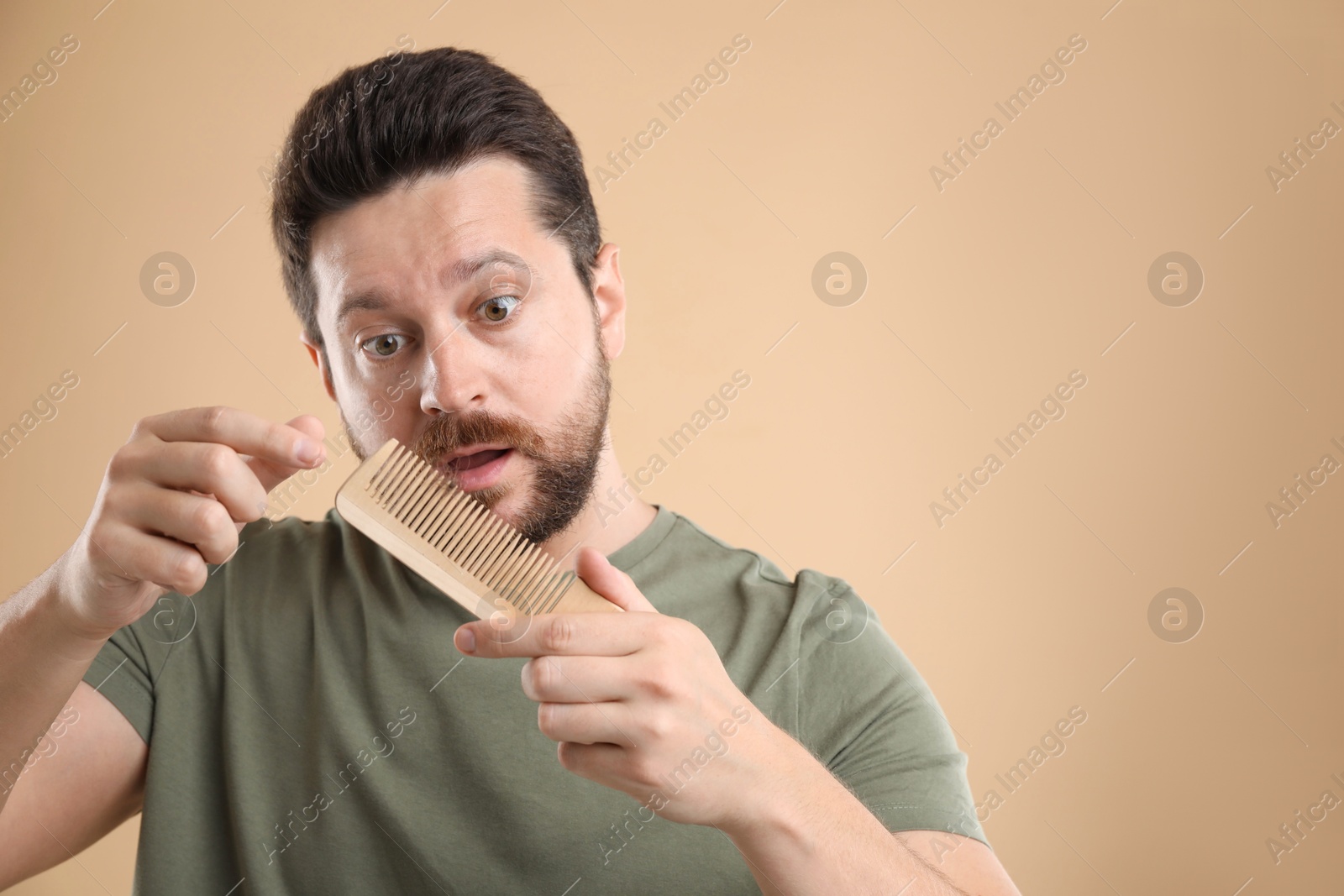 Photo of Sad man taking his lost hair from comb on beige background, space for text. Alopecia problem