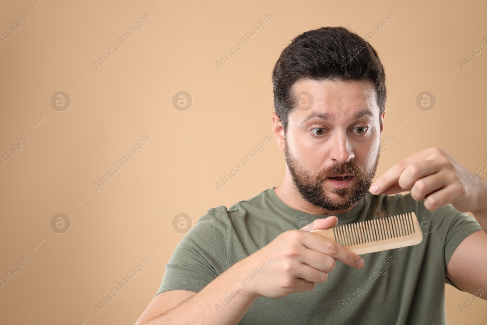 Photo of Sad man taking his lost hair from comb on beige background, space for text. Alopecia problem