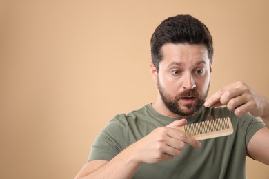 Sad man taking his lost hair from comb on beige background, space for text. Alopecia problem