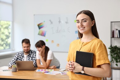 Happy young designer with notebook in office