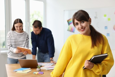 Portrait of happy young designer with notebook in office