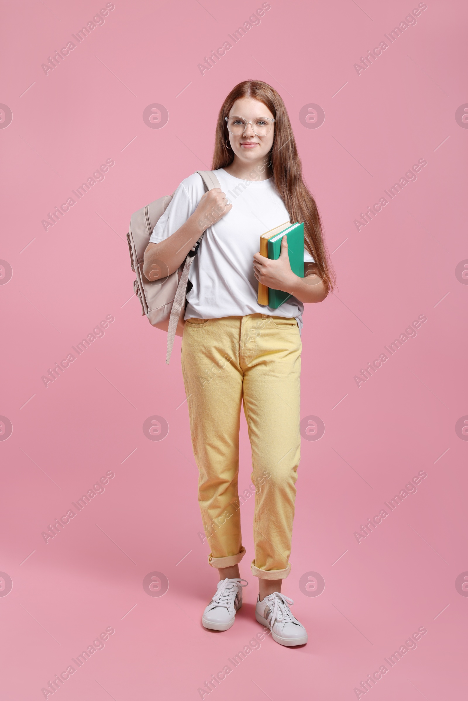 Photo of Teenage girl with backpack and books on pink background