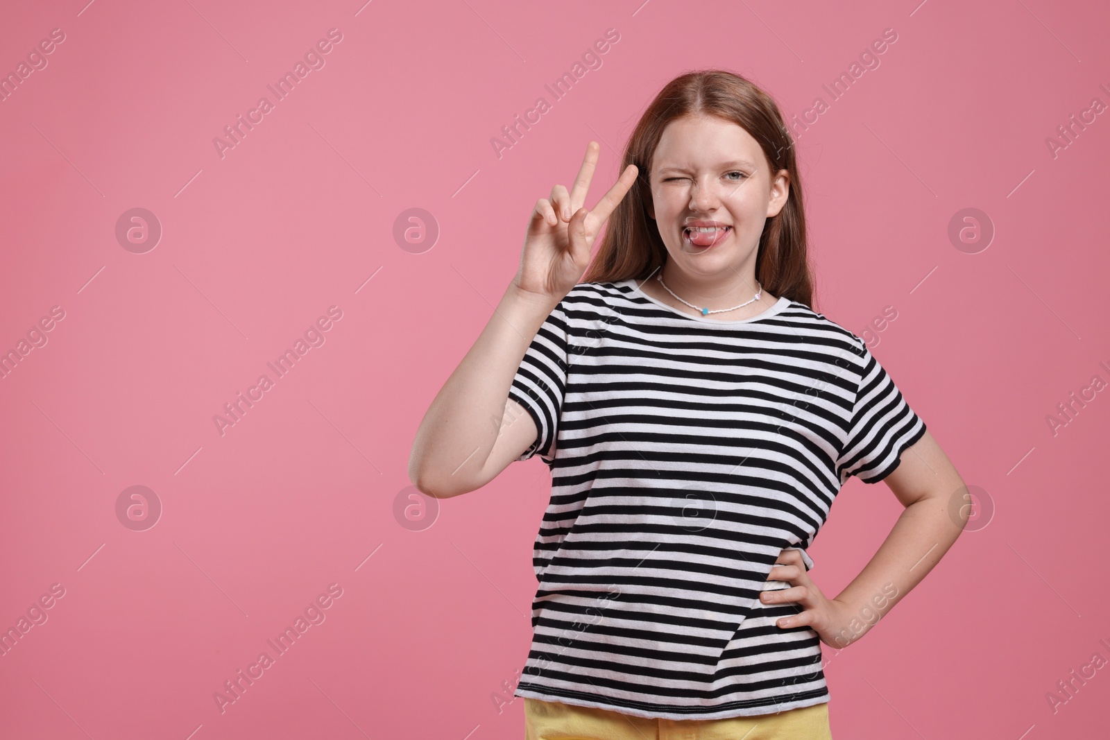 Photo of Teenage girl with showing tongue and v-sign on pink background, space for text