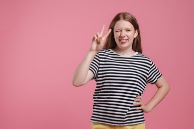 Teenage girl with showing tongue and v-sign on pink background, space for text