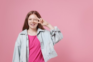 Photo of Teenage girl with showing v-sign on pink background, space for text