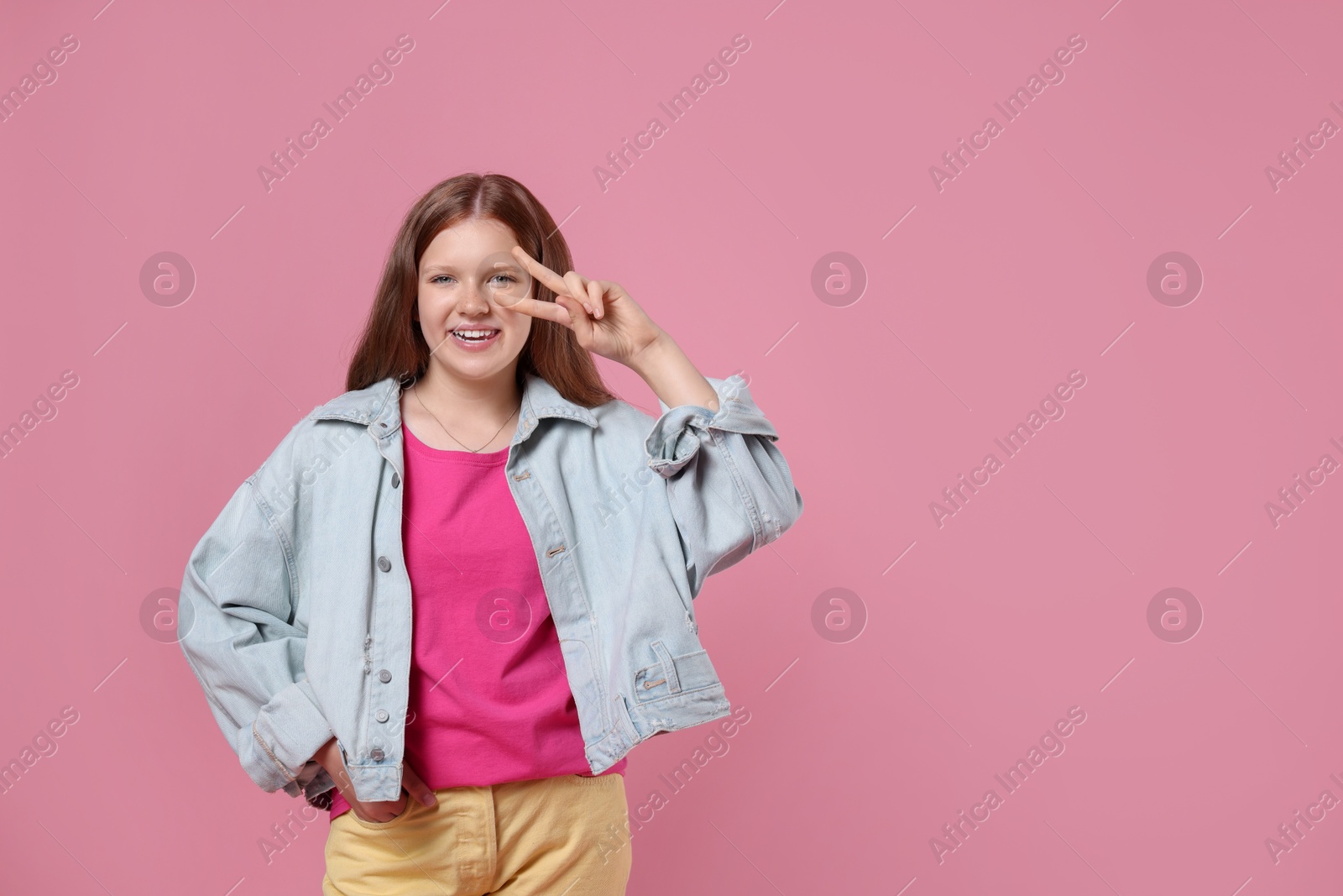 Photo of Teenage girl with showing v-sign on pink background, space for text