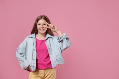 Teenage girl with showing v-sign on pink background, space for text