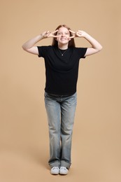 Teenage girl with showing v-sign on beige background