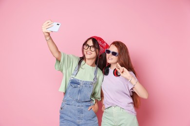 Photo of Happy teenage girls taking selfie on pink background