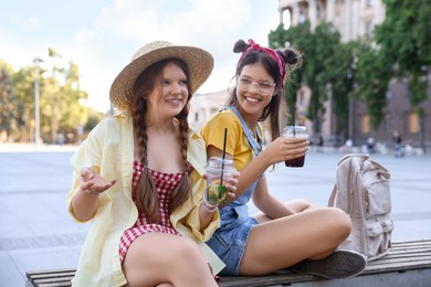 Happy teenage friends sitting on bench outdoors