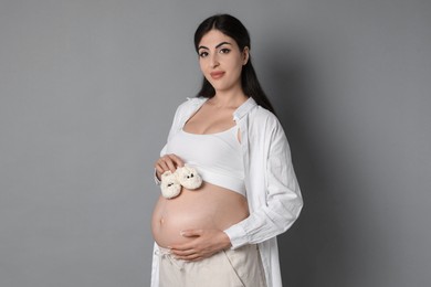 Portrait of beautiful pregnant woman with baby shoes on grey background