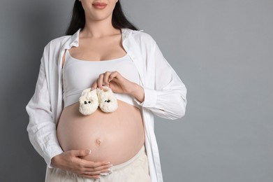 Young pregnant woman with pair of baby shoes on grey background, closeup. Space for text