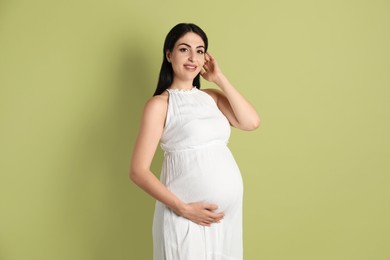 Portrait of beautiful pregnant woman on light olive background