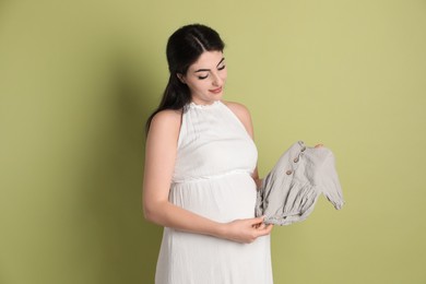 Photo of Portrait of beautiful pregnant woman with baby onesie on light olive background