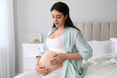 Photo of Young pregnant woman sitting on bed at home