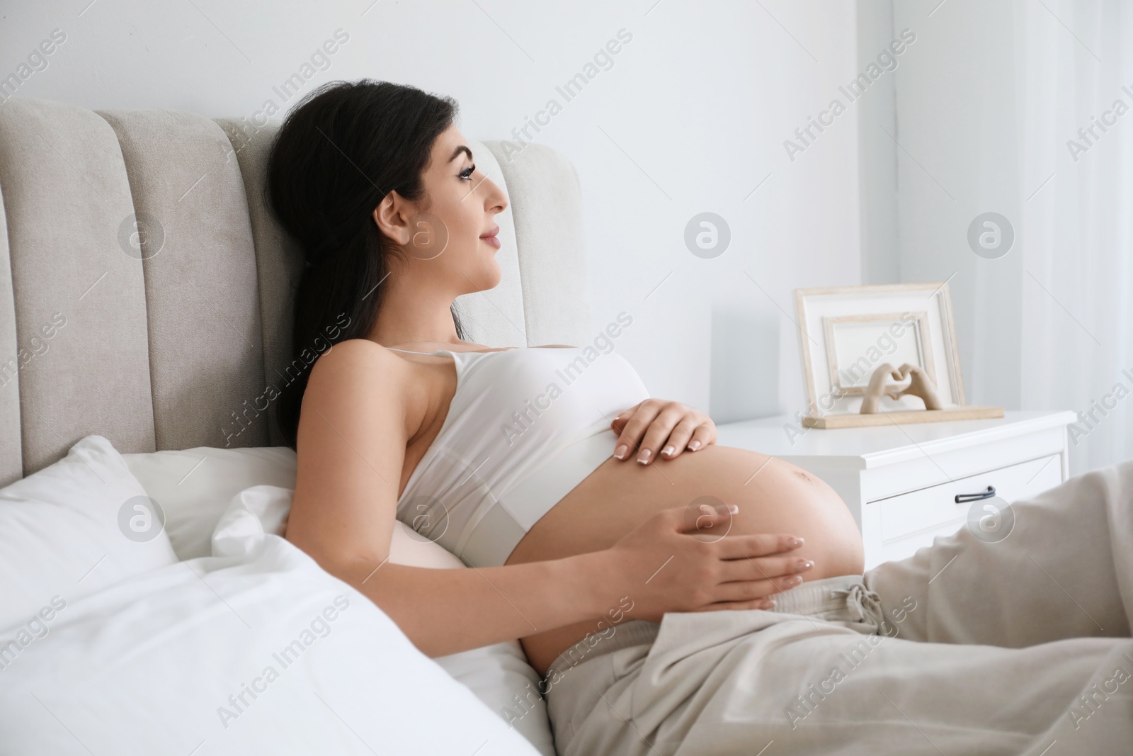 Photo of Young pregnant woman lying on bed at home