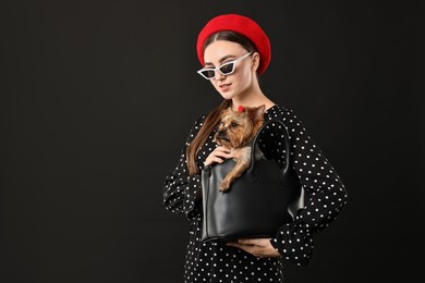 Woman in sunglasses holding bag with cute Yorkshire Terrier dog on black background