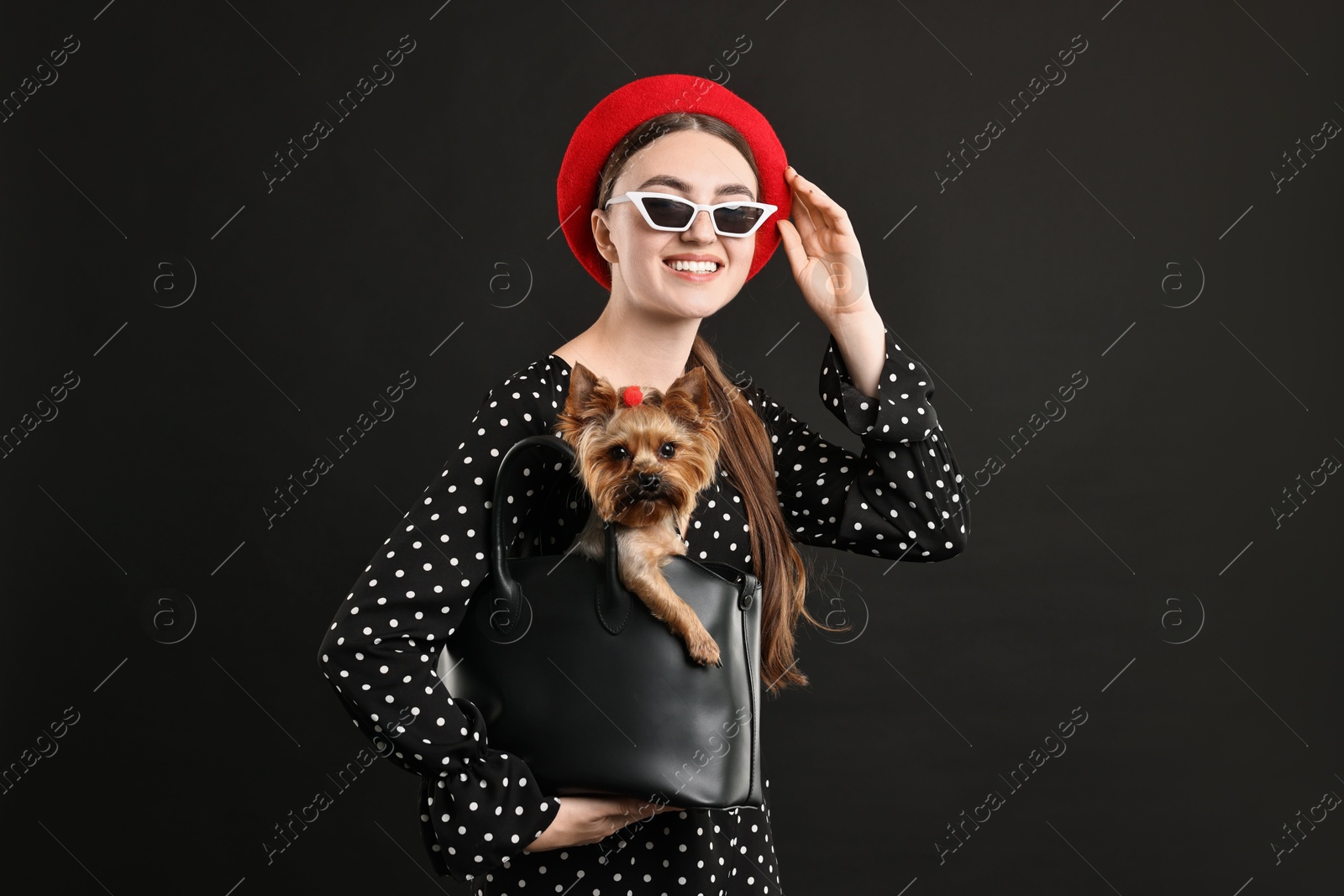 Photo of Woman in sunglasses holding bag with cute Yorkshire Terrier dog on black background