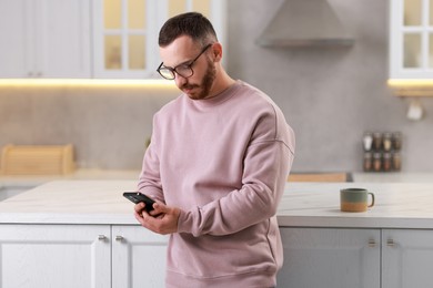 Handsome man looking at smartphone in kitchen