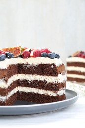 Delicious chocolate sponge cake with berries on white wooden table, closeup