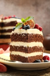 Photo of Piece of delicious chocolate sponge cake with berries on wooden table, closeup