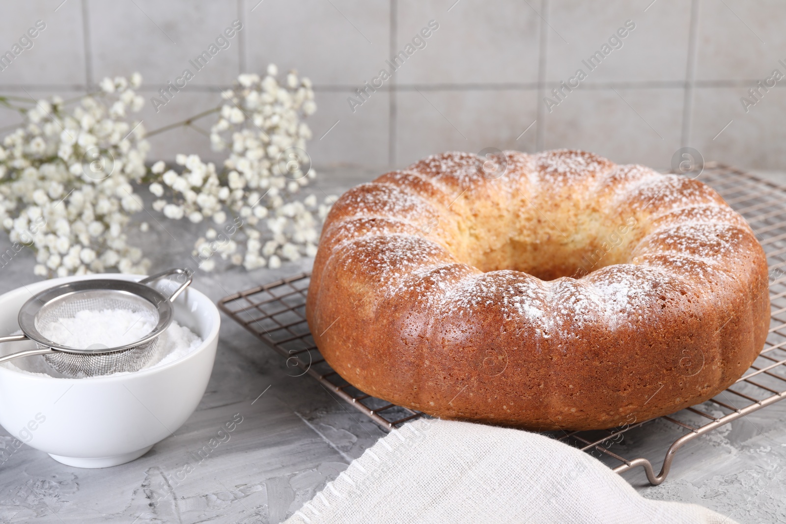 Photo of Freshly baked sponge cake with powdered sugar and flowers on grey table, closeup