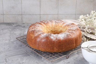 Photo of Freshly baked sponge cake with powdered sugar and flowers on grey table, closeup