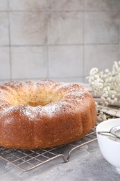 Freshly baked sponge cake with powdered sugar and flowers on grey table, closeup