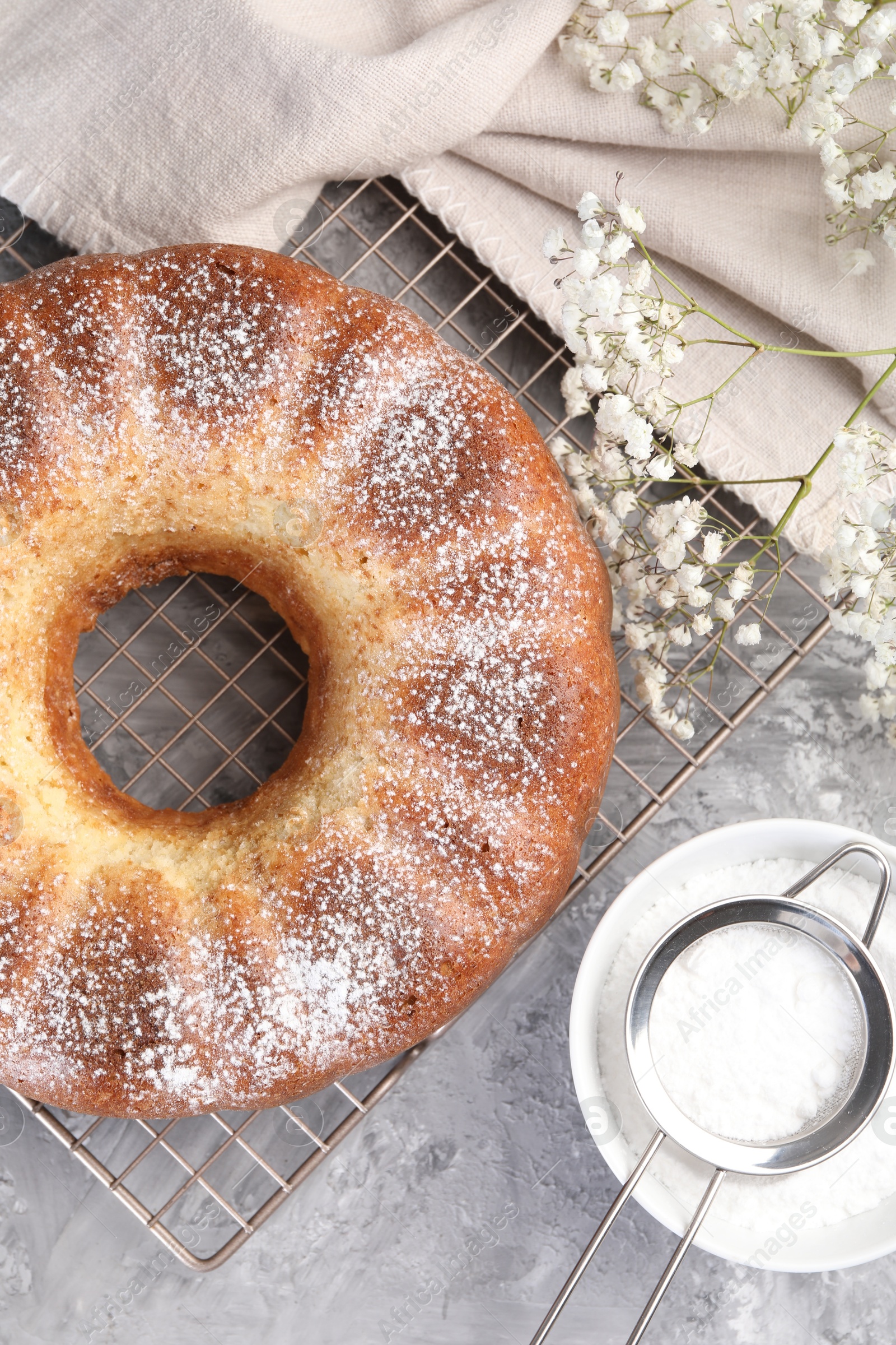 Photo of Freshly baked sponge cake with powdered sugar and flowers on grey table, top view