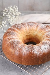 Photo of Freshly baked sponge cake with powdered sugar on grey table, closeup