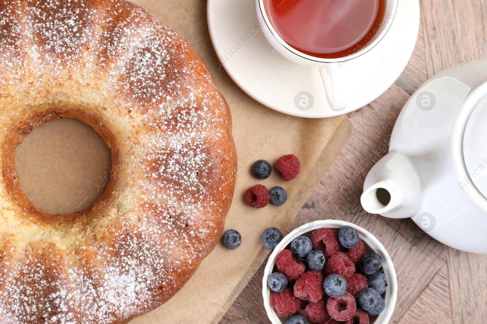 Photo of Freshly baked sponge cake, tea and berries on wooden table, top view