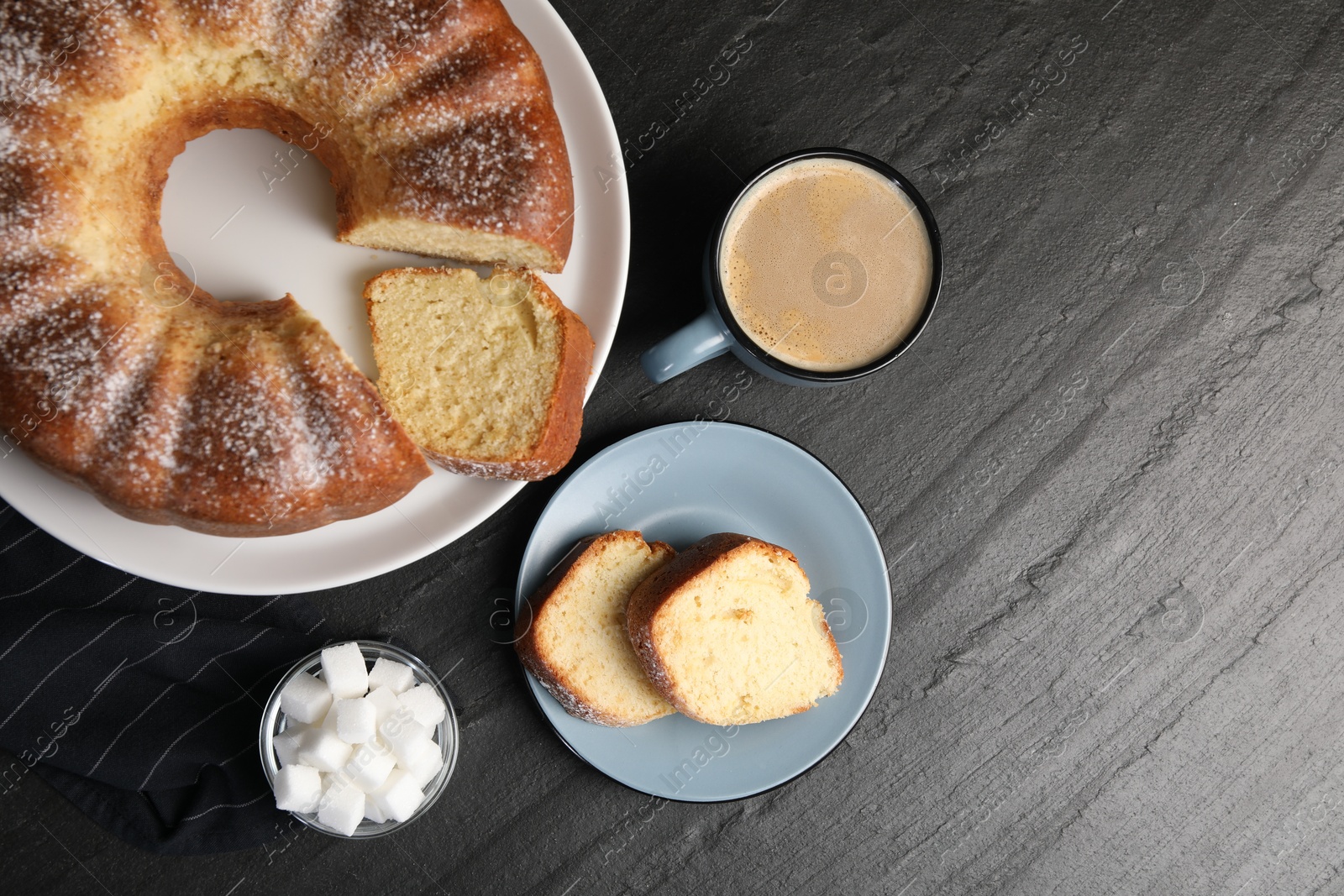 Photo of Freshly baked sponge cake, sugar cubes and coffee on black table, top view