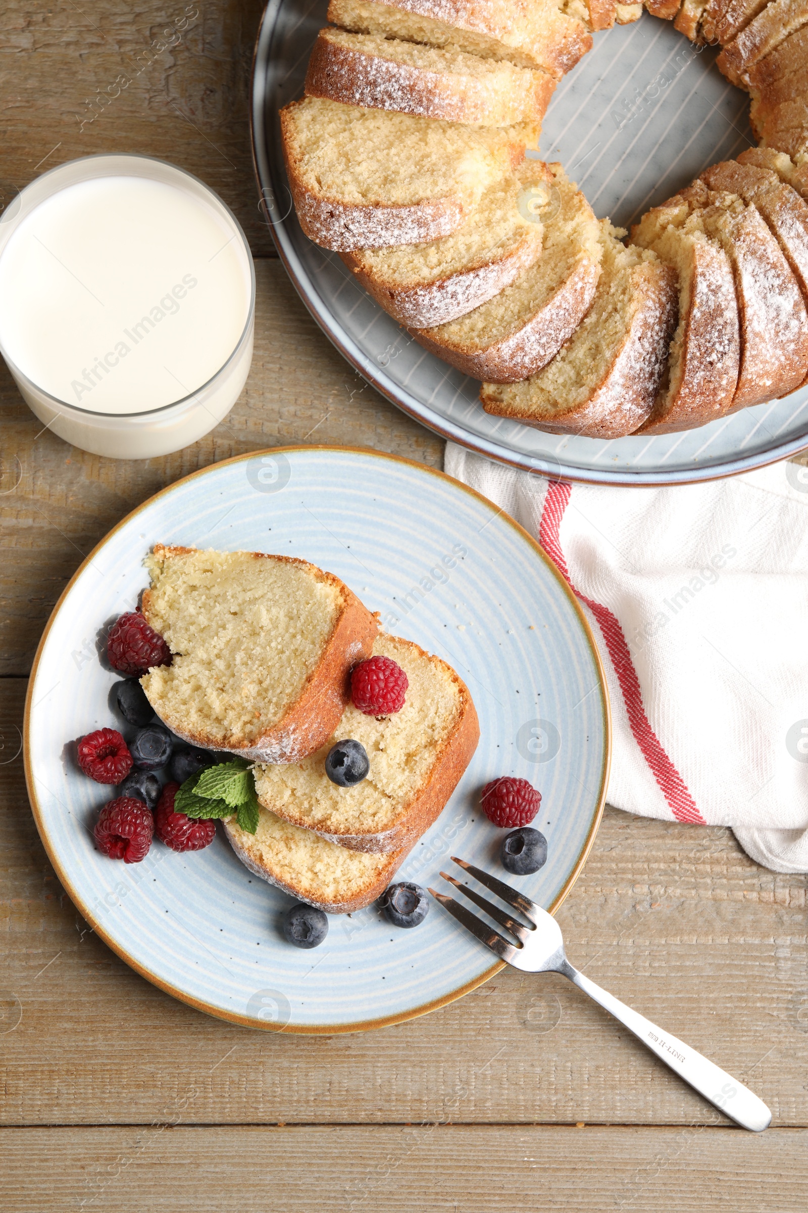 Photo of Pieces of freshly baked sponge cake, berries and milk on wooden table, flat lay