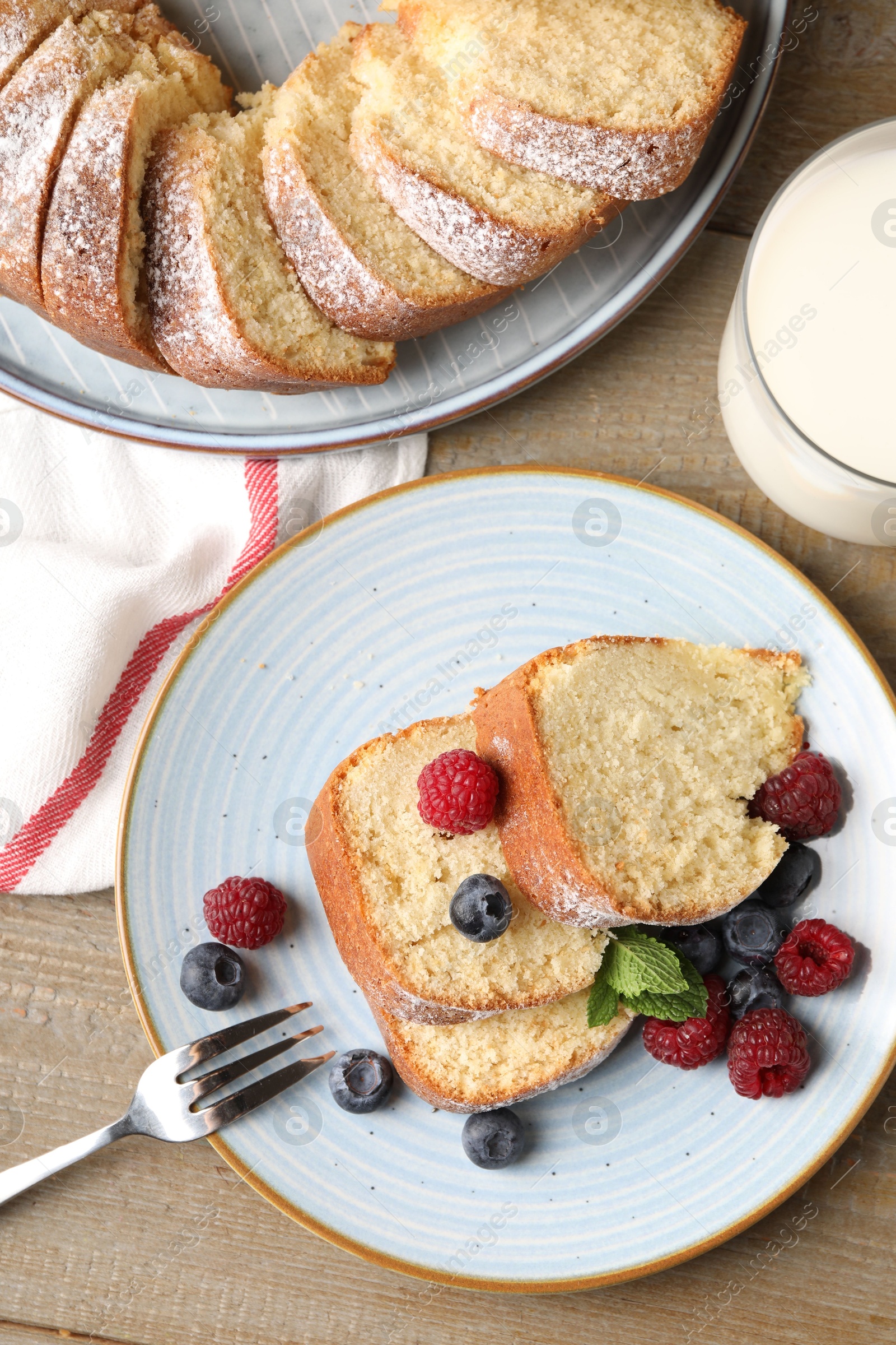 Photo of Pieces of freshly baked sponge cake, berries and milk on wooden table, flat lay