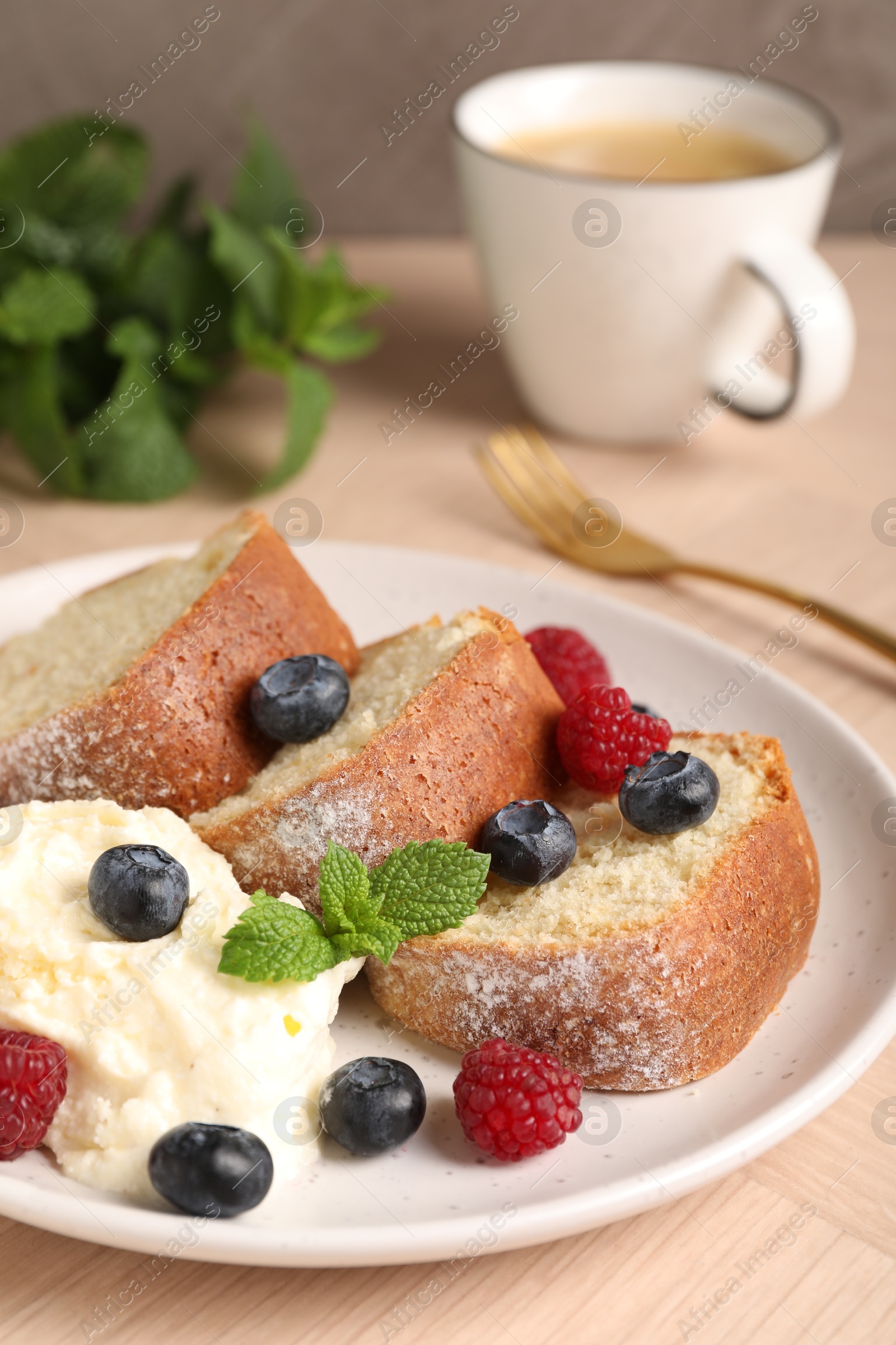 Photo of Pieces of freshly baked sponge cake, berries, ice cream, mint and coffee on wooden table, closeup