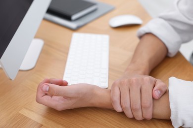 Photo of Man suffering from pain in wrist while working on computer at table indoors, closeup. Carpal tunnel syndrome