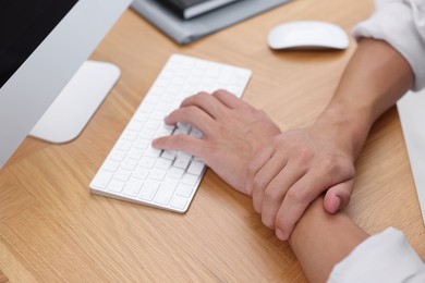 Photo of Man suffering from pain in wrist while working on computer at table indoors, closeup. Carpal tunnel syndrome