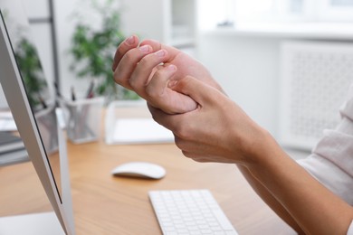 Photo of Man suffering from pain in wrist while working on computer at table indoors, closeup. Carpal tunnel syndrome