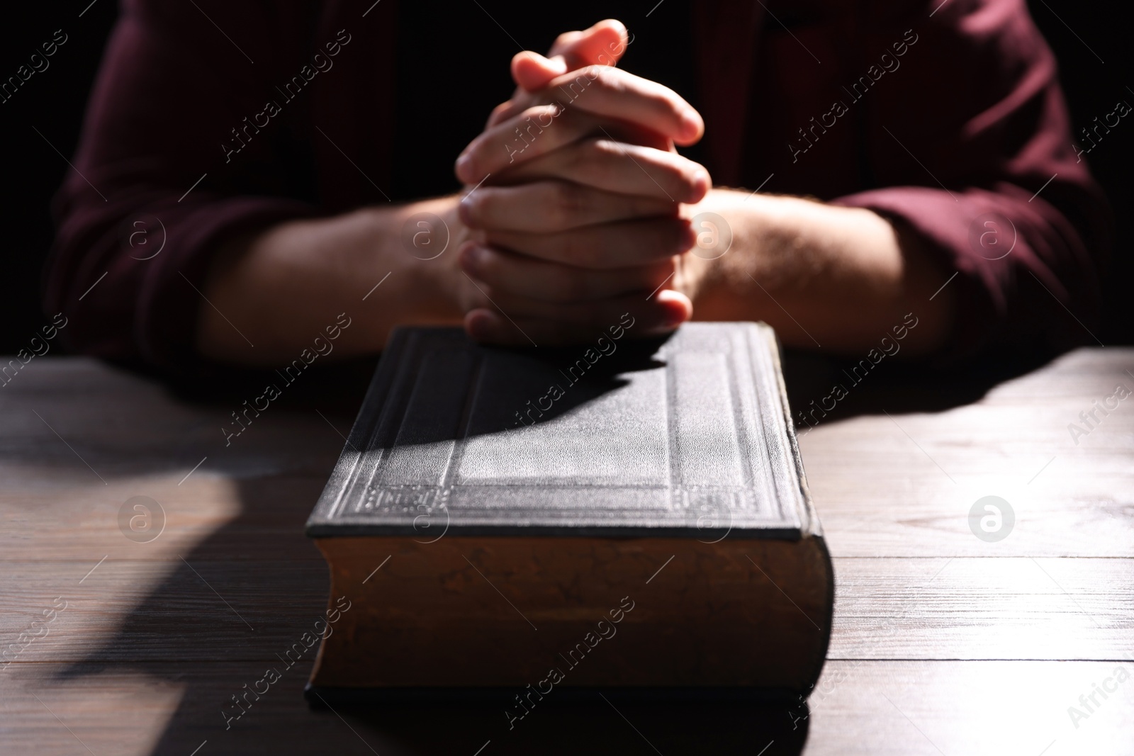 Photo of Man with Bible praying at wooden table, closeup