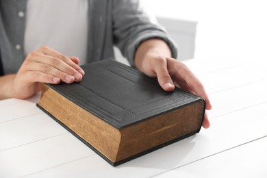 Photo of Man with Bible at white wooden table, closeup