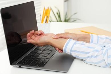 Photo of Carpal tunnel syndrome. Woman suffering from pain in wrist at desk indoors, closeup