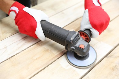 Man polishing wooden planks with angle grinder outdoors, closeup