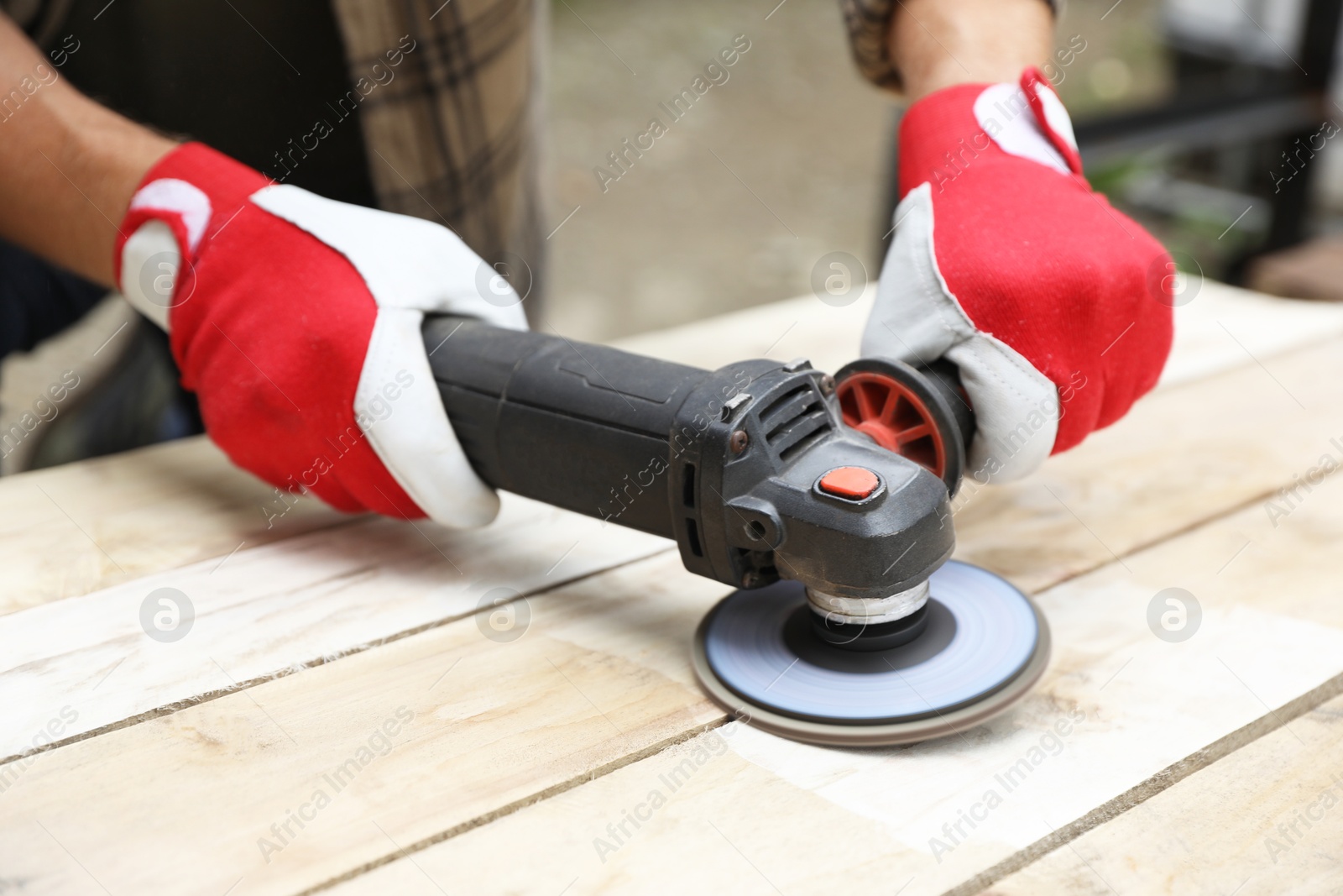 Photo of Man polishing wooden planks with angle grinder outdoors, closeup