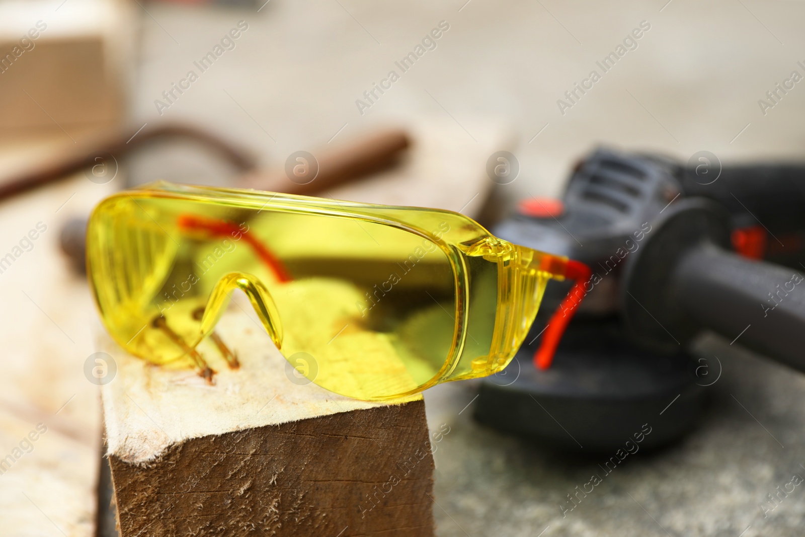 Photo of Protective goggles, nails, wooden plank and angle grinder outdoors, closeup