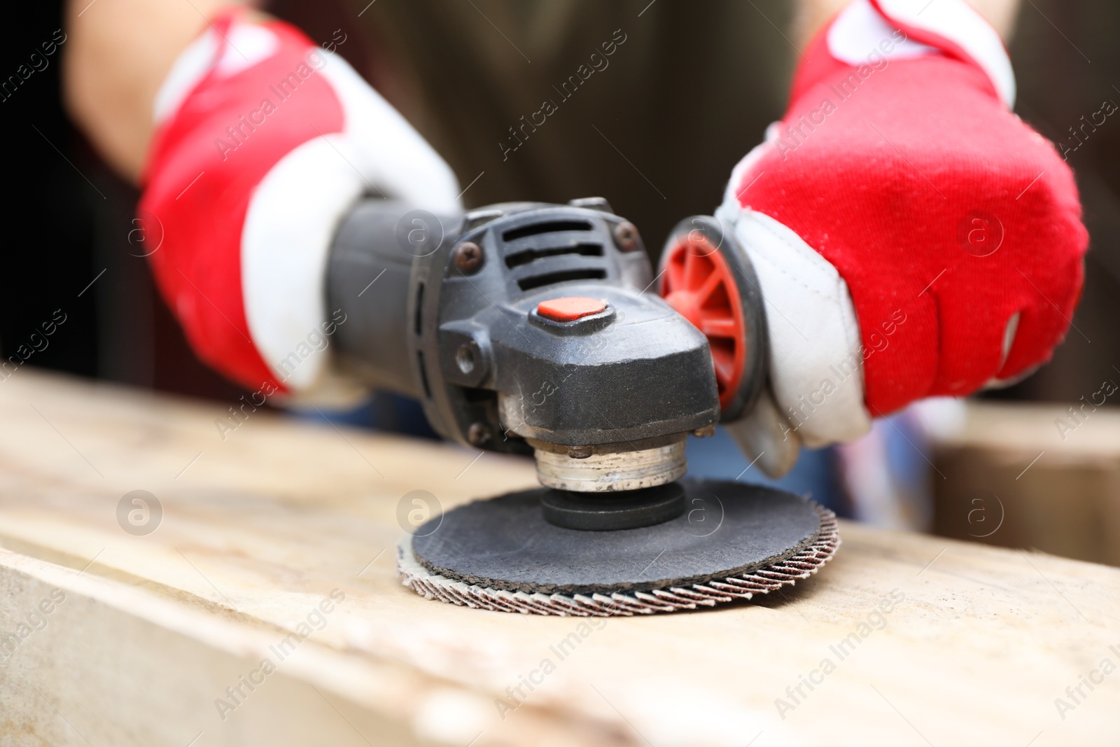 Photo of Man polishing wooden planks with angle grinder outdoors, closeup