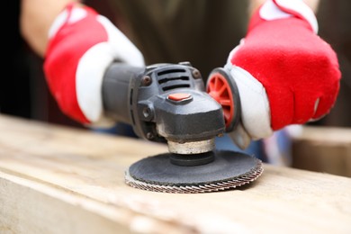 Photo of Man polishing wooden planks with angle grinder outdoors, closeup