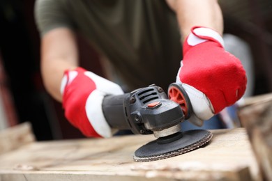 Photo of Man polishing wooden planks with angle grinder outdoors, closeup