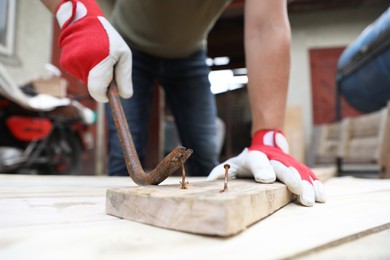 Man pulling metal nail out of wooden plank with crowbar outdoors, closeup