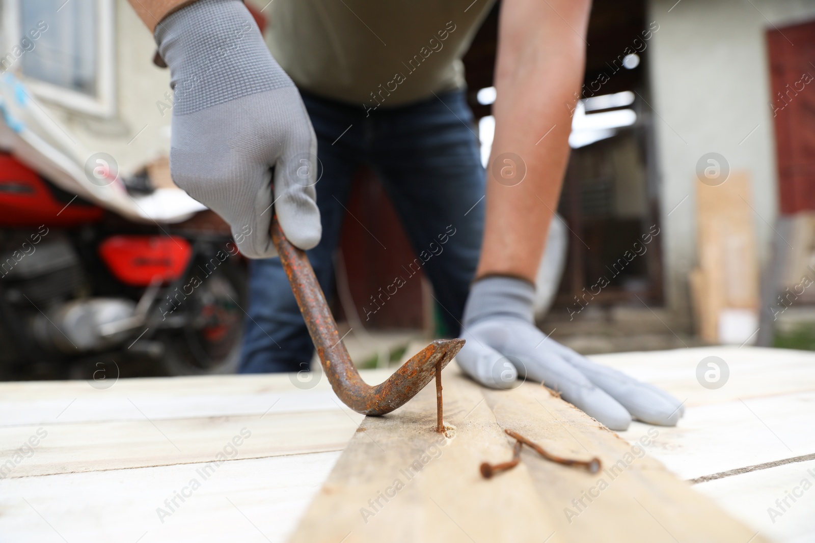 Photo of Man pulling metal nail out of wooden plank with crowbar outdoors, closeup